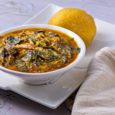 Close up of Nigerian food, Oha soup with beef served with garri on a white plate placed with linen fabric.
