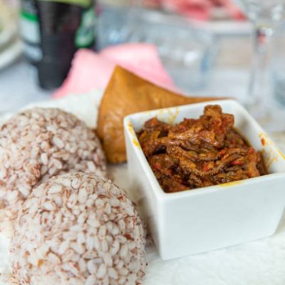A dish of ofada rice and sauce with moi moi about to be given t a guest an event