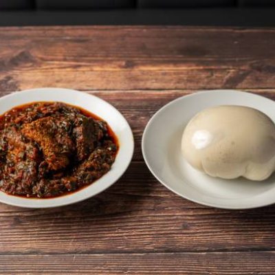 A plate of traditional African vegetable soup with meat served alongside a plate of fufu on a wooden table.